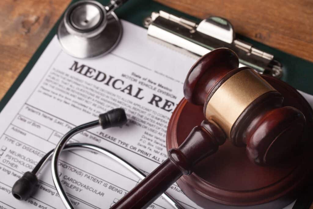 Stethoscope and gavel resting on a medical report | medical malpractice attorneys​ | Menzer Law|A lawyer and client are seated at a desk | best personal injury attorneys​ | Menzer Law|A person on a couch with a broken leg | medical malpractice law firm​​ | Menzer Law