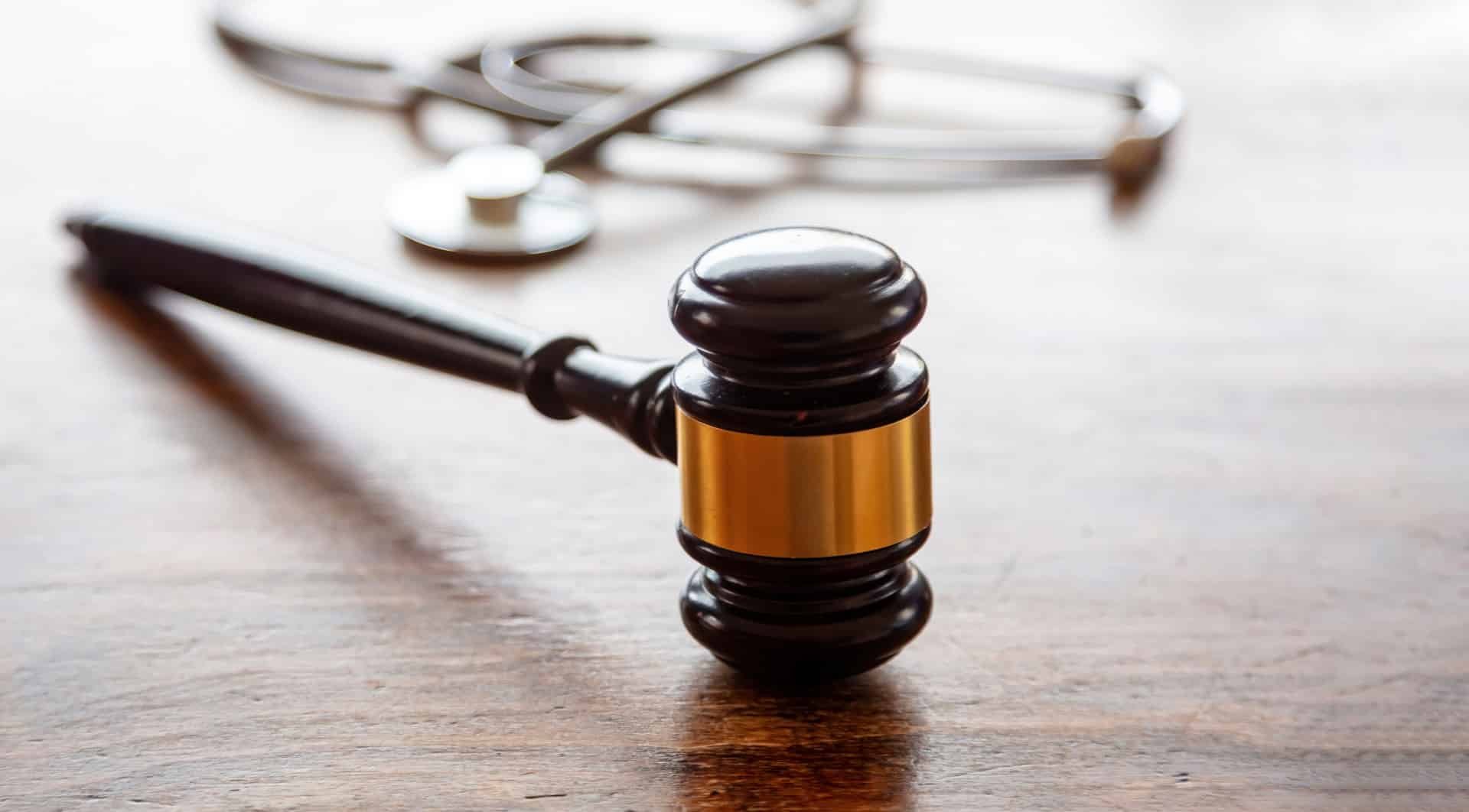 Judge's gavel and stethoscope on a wooden table | hospital negligence lawyers​ | Menzer Law|A new mother in a hospital gown holds her newborn | hospital negligence lawyers​ | Menzer Law|Lawyer in court