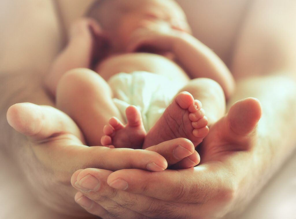 Close-up of a baby's feet cradled in adult hands | medical malpractice attorneys​ | Menzer Law|Person holding a baby wrapped in a white fluffy blanket | life insurance lawyer​ | Menzer Law|Newborn baby sleeping in a clear hospital bassinet | medical malpractice attorneys​ | Menzer Law