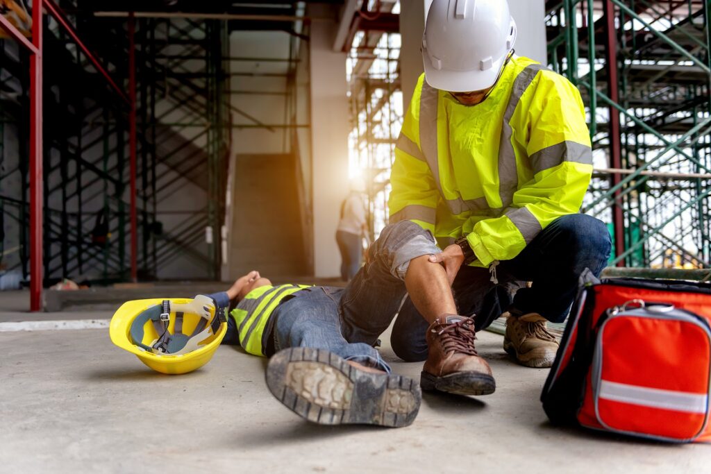 Construction worker giving first aid to a colleague | personal injury attorney​ | Menzer Law|A man in an orange vest repairs a control panel | personal injury law firm​ | Menzer Law|Two people engaged in a handshake across a table | personal injury attorney​ | Menzer Law