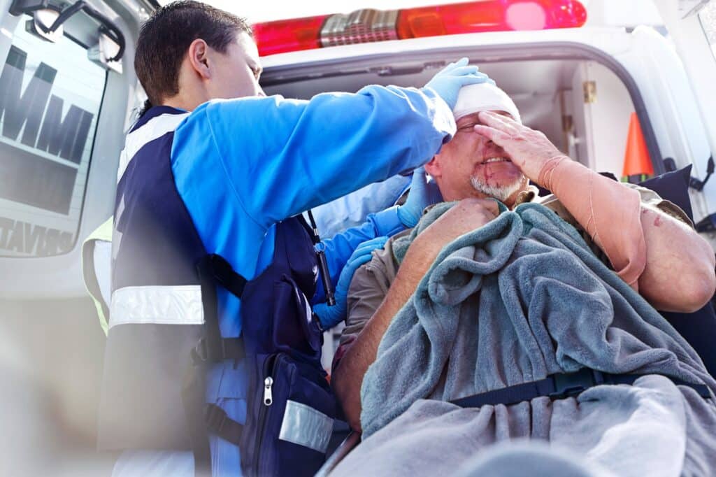 A man with a head injury getting loaded into the back of an ambulance on a stretcher.