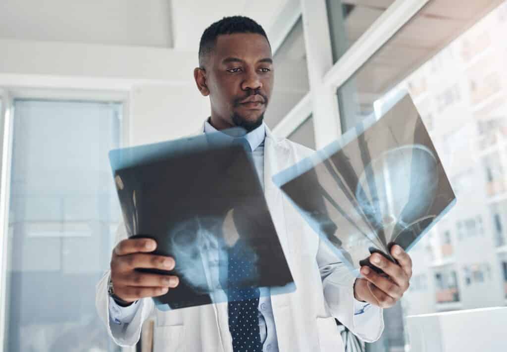 A doctor standing in a hospital room holding two head x-rays.