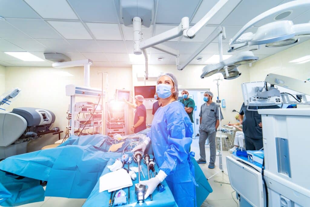 A doctor reaching for medical tools in a busy emergency room next to a stretcher.