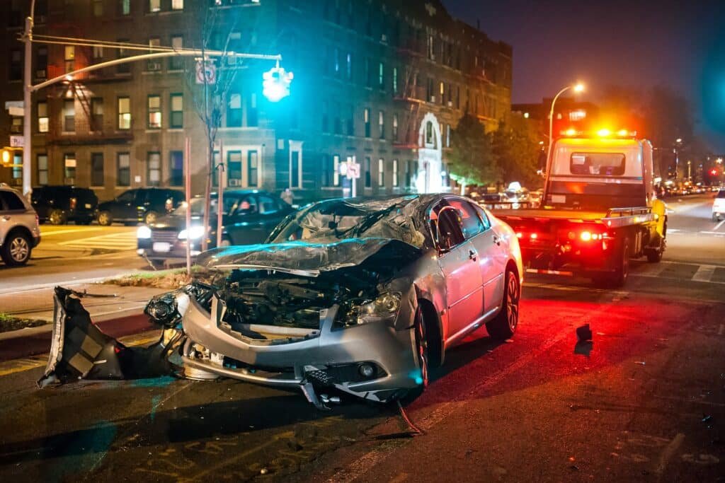 A wrecked car next to a tow truck in a city intersection at night.