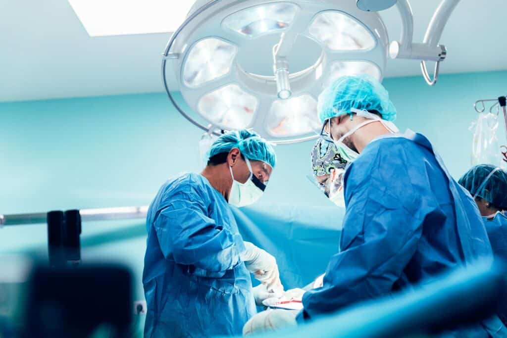 Three surgeons working on a patient under a large light in a hospital.