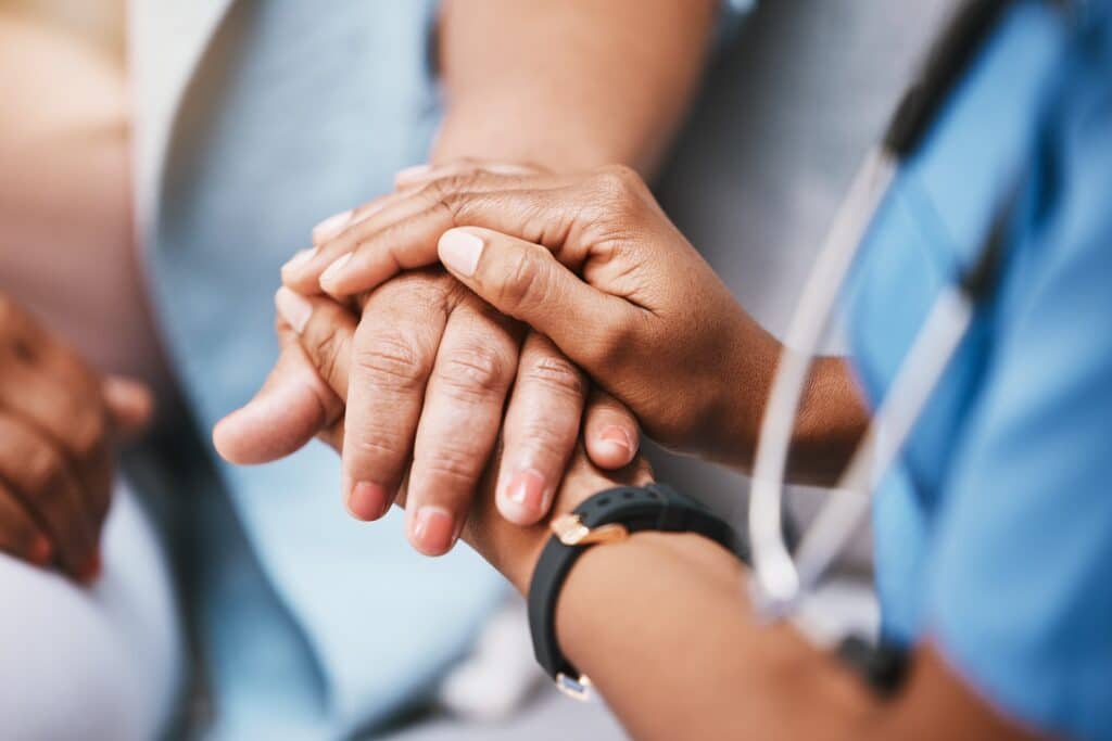 A nurse holds a patient's hand between both of her hands.