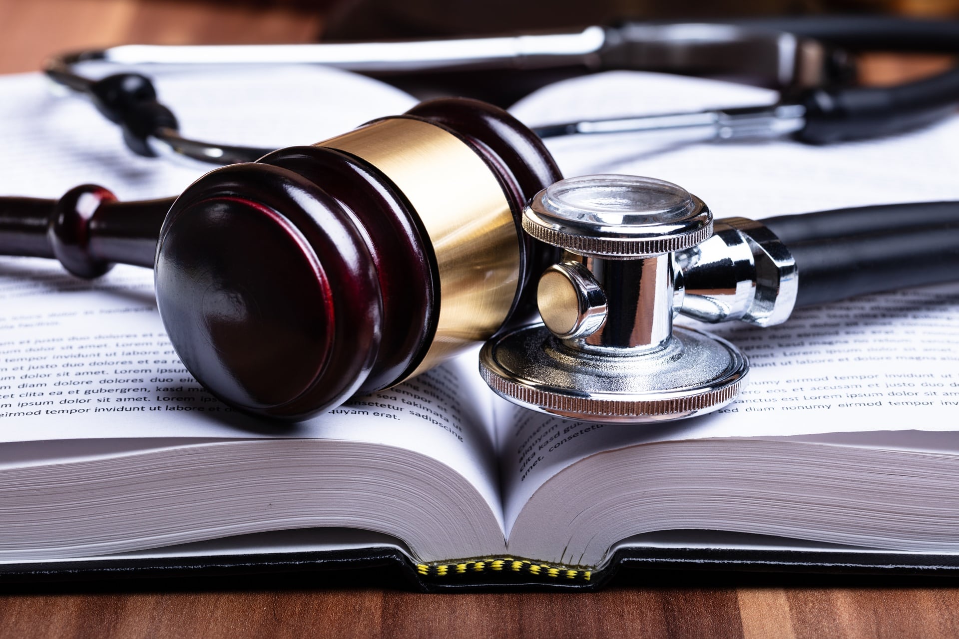 A gavel resting on an open medical book next to a stethoscope.