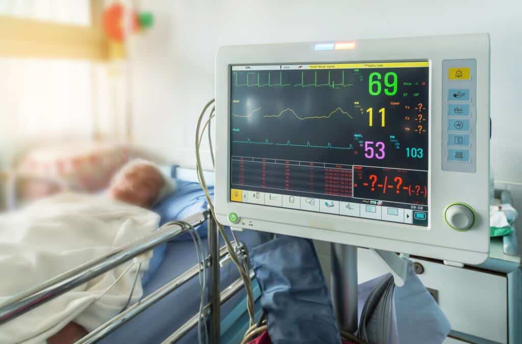A person lays in a hospital bed next to a display showing their vitals.