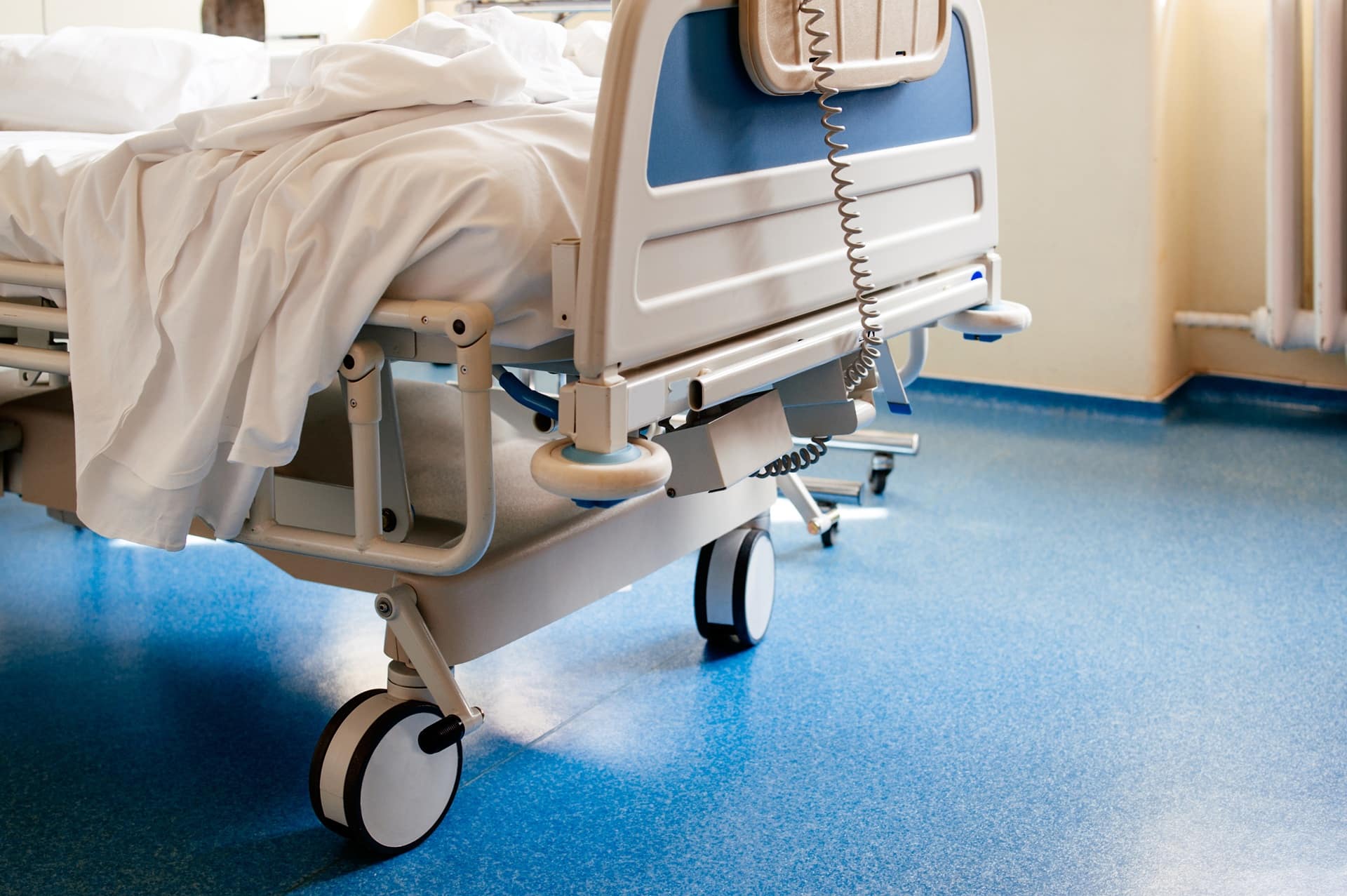 A hospital bed with large wheels on and a blanket on it sitting on a blue floor.