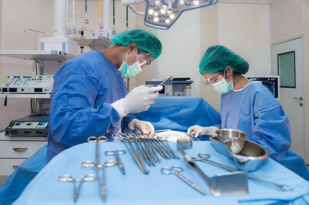 Two surgeons look over a patient in a hospital next to an assortment of surgical tools.