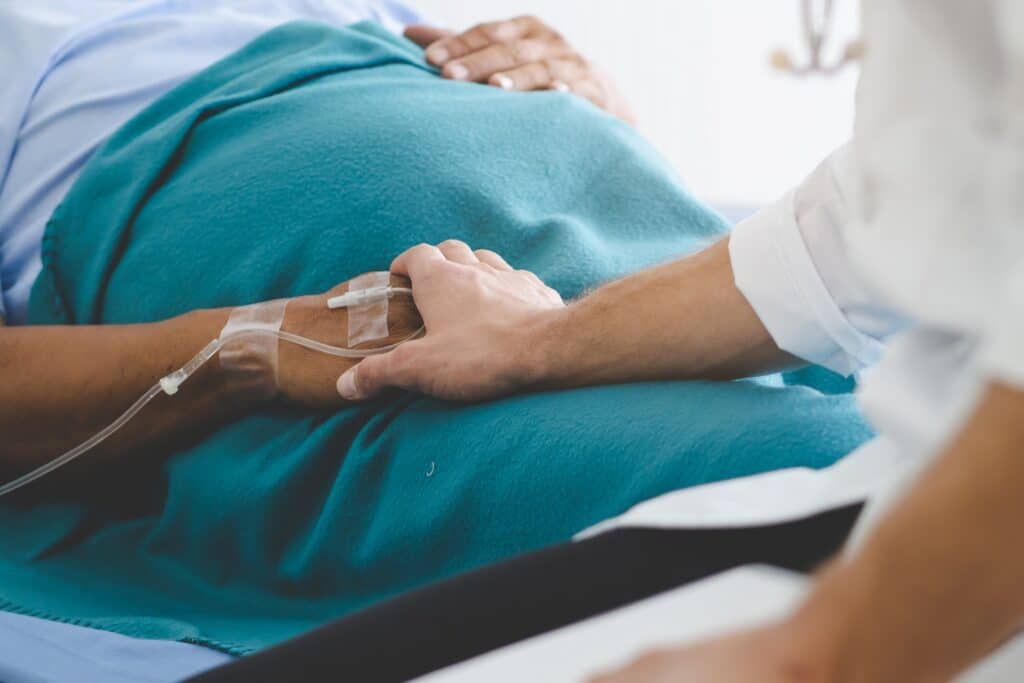 A person holding the hand of a patient laying in a hospital bed.