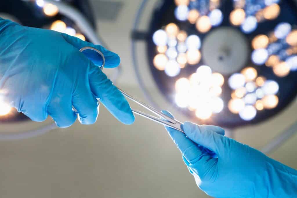 A surgeon hands a tool to another surgeon in a hospital.