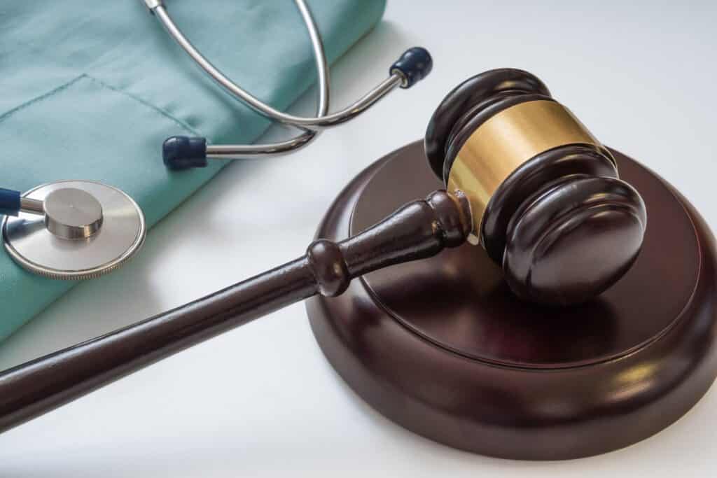 A gavel resting on its stand next to a stethoscope sitting on scrubs.