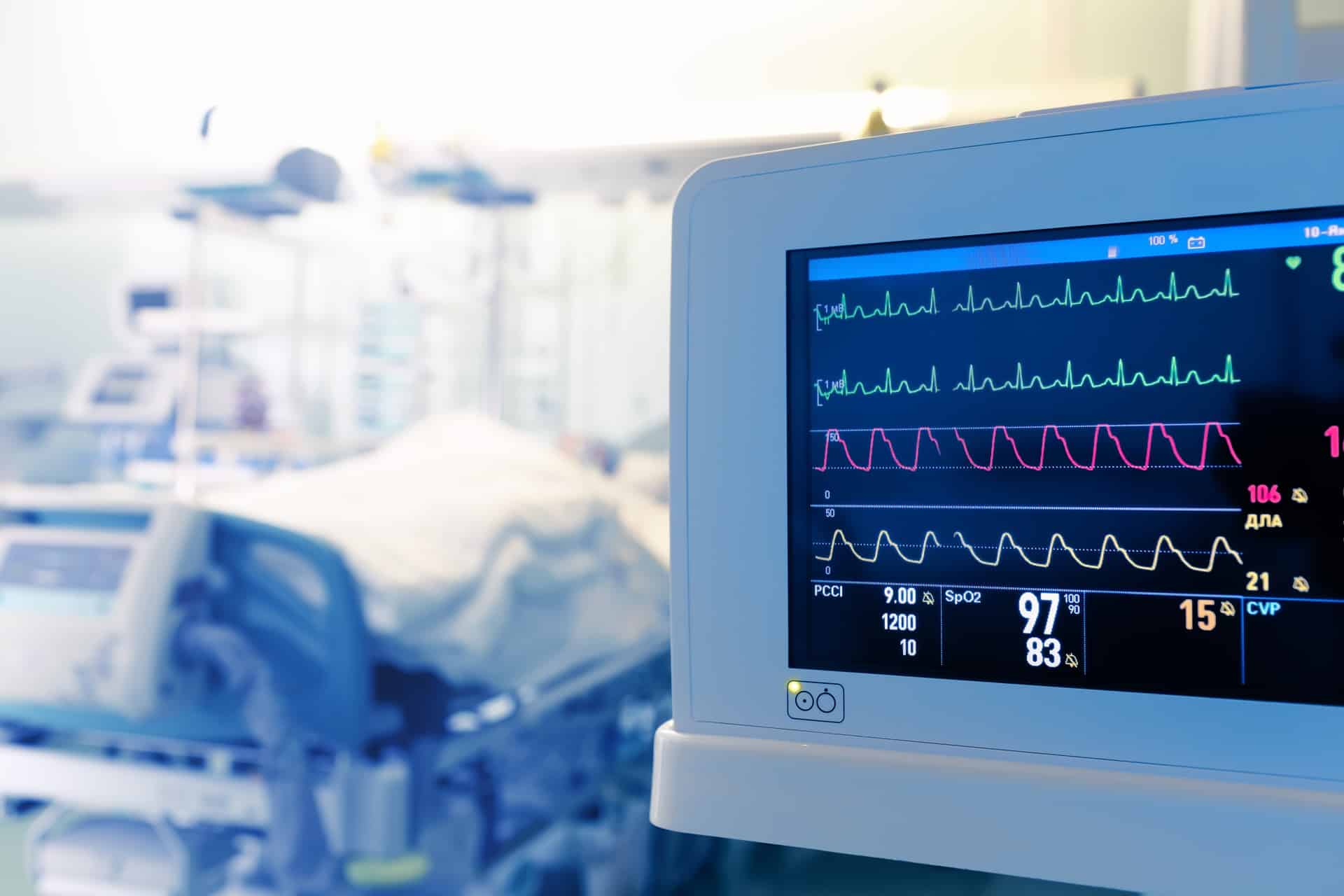 A hospital bed sitting next to a monitor showing vitals.