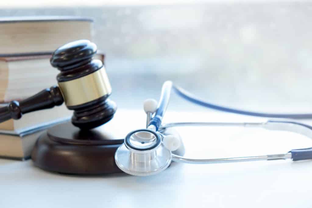 A gavel resting on its stand next to a stethoscope and some books.