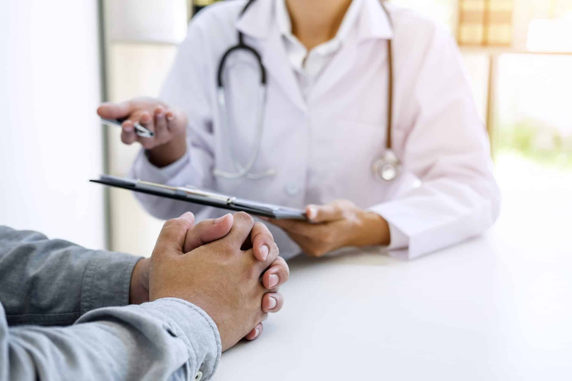 A doctor sitting across a desk from a patient holding a clipboard.