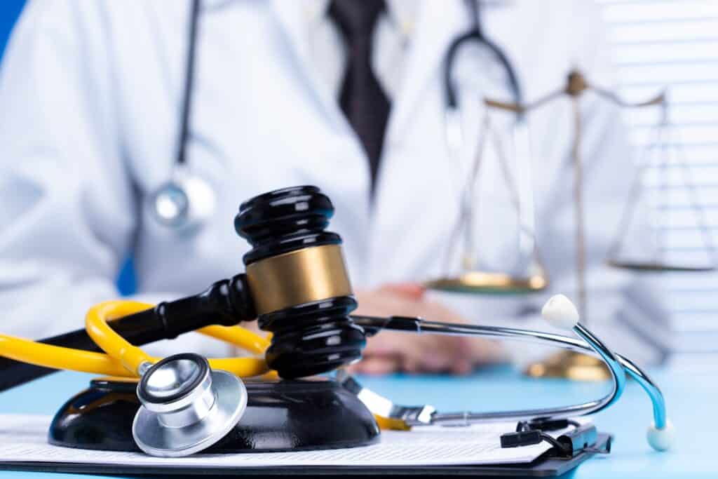 A gavel rests on its stand next to a stethoscope on a desk in front of a doctor.