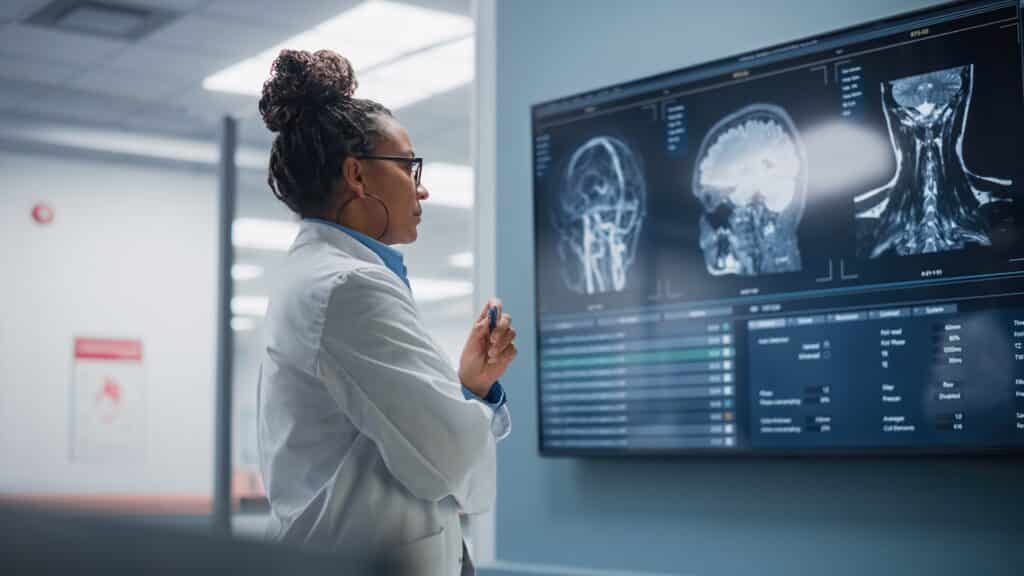 A female doctor looks at x-ray scans of a person's head on the wall of a hospital.