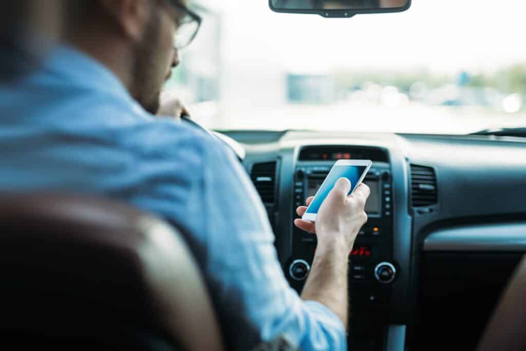 A man looks at his cell phone while behind the wheel of a moving vehicle.