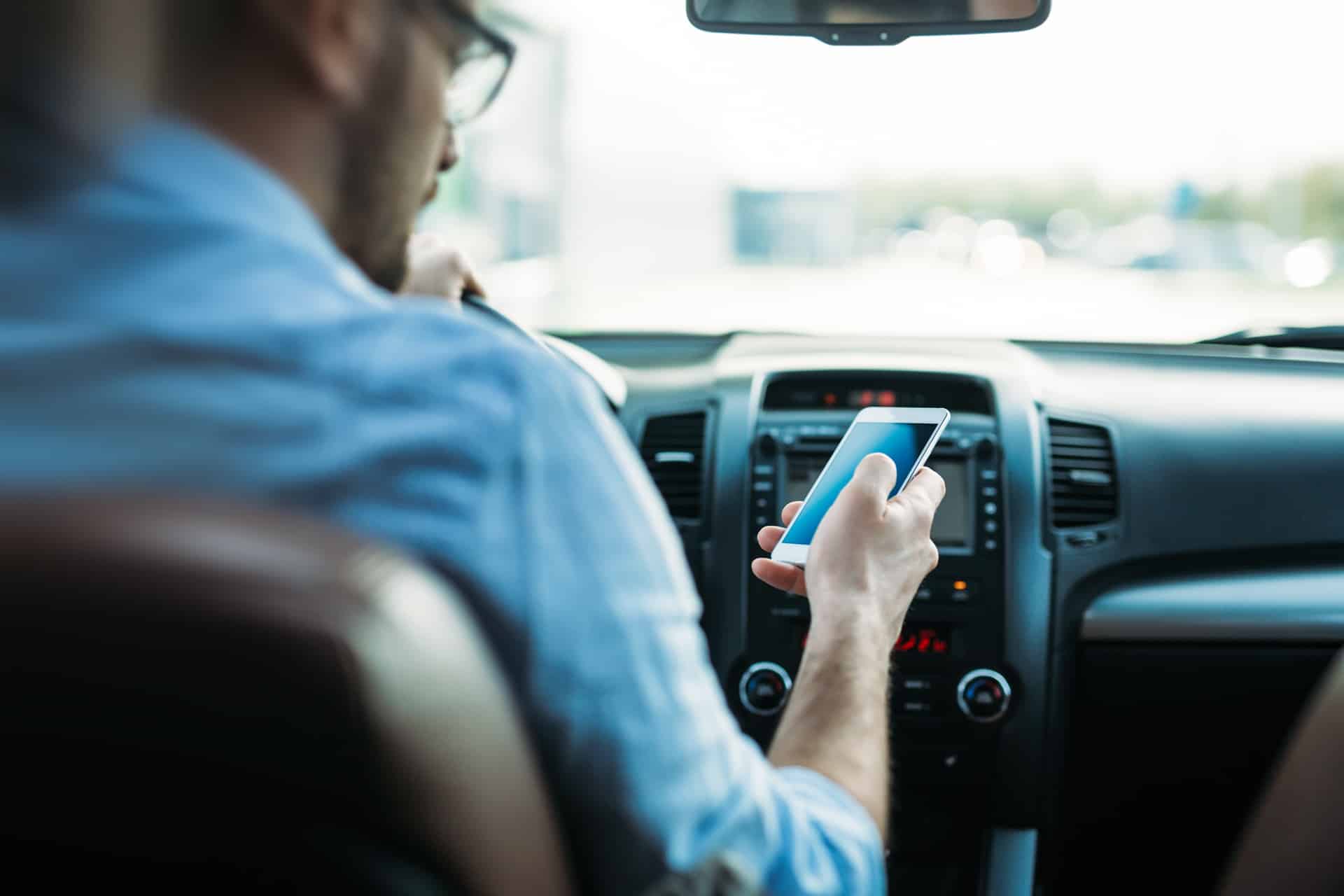 A man looks at his cell phone while behind the wheel of a moving vehicle.