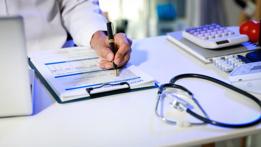 A doctor writes on medical records on a clipboard next to a stethoscope.