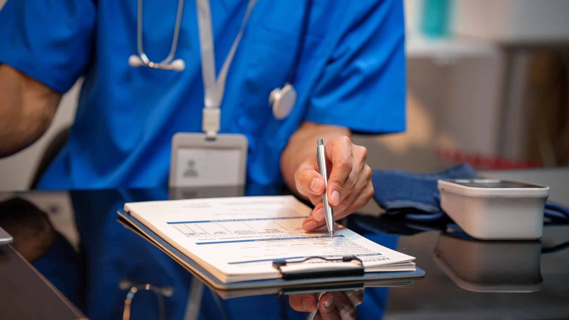 A medical professional reviews a chart on a clipboard in a hospital.